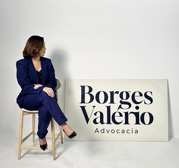Dra. Fabiana Borges Valério sentada num banco alto ao lado da placa Borges Valério Advocacia